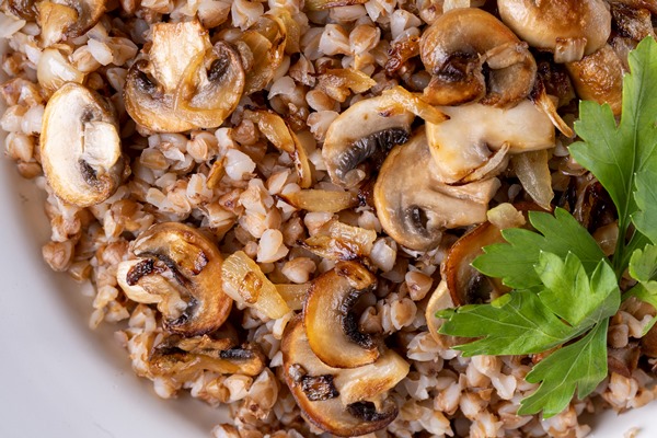 buckwheat porridge with mushrooms in a white plate on wooden background - Гречневые тефтели с грибами и зеленью