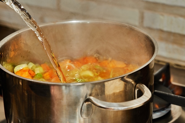 cook pours water into pan with onions carrots and leeks on gas stove - Овощи, бобовые, грибы: полезные советы