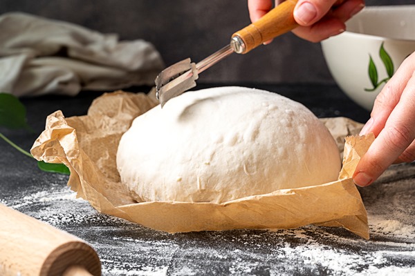 cooking sourdough bread at home female hand cutting freshly risen bread dough witha lame getting ready for baking - О полезном домашнем хлебе