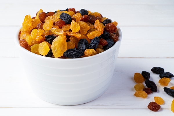 different varieties of raisins in a bowl on a white wooden background side view - Сочиво