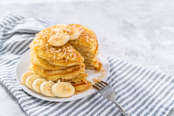 eating freshly baked coconut banana pancakes garnished with sliced bananas and toasted coconut - Толстые блины на манке и геркулесе