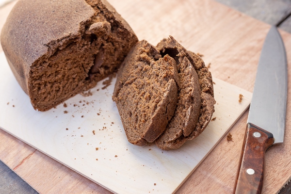 freshly baked brown borodino bread bun cut into slices next to a large knife fresh homemade baked goods selective focus - Домашний хлебный квас