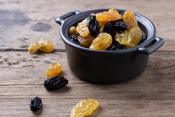 golden and black raisins on wooden table background - Постный овсяный десерт с орешками и сухофруктами