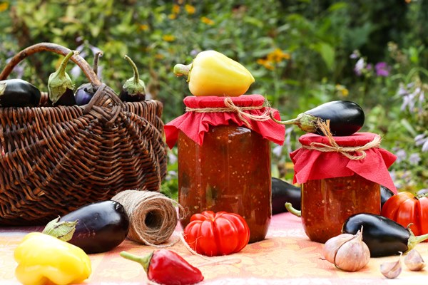 homemade adzhika and eggplants in tomatoes sause in jars located on a table in the garden - Аджика с яблоками