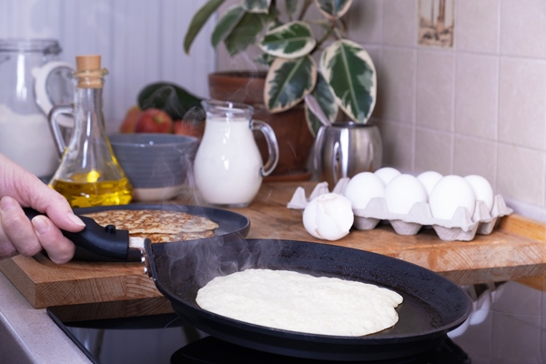 housewife woman bakes pancakes for breakfast home cooking pancakes in pan on glassceramic stove in her kitchen diy ingredients for making pancakes selective focus - Толстые блины на манке и геркулесе