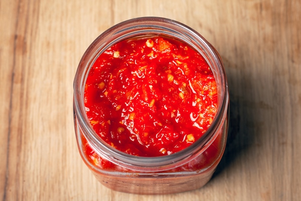 jar with red chili pepper and tomato sauce caucasian traditional adjika sauce on wooden table - Аджика с яблоками
