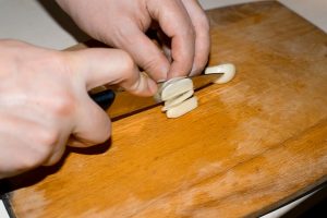 male hands chop peeled garlic on a wooden cutting board close up - Огурцы солёные с красной смородиной