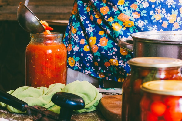 man in a colored apron clogs tomatoes and lecho sauce in glass jars in a farmhouse - Лечо двухцветное с душистыми травами