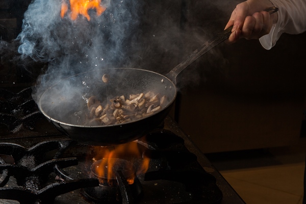 side view mushroom frying with smoke and fire and human hand and pan in stove - Жареные опята на зиму