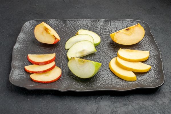 side view of several types of sliced fresh apples on a black tray on a dark background - Аджика с яблоками