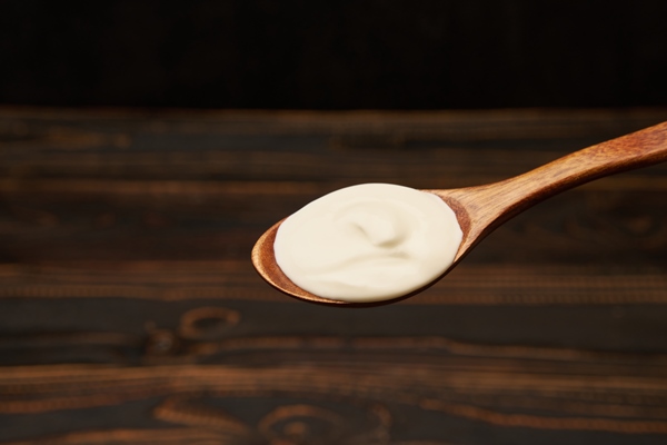 sour cream in wooden spoon over wooden background - Запеканки в духовке: правила приготовления