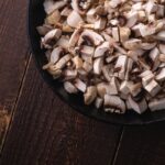 tasty chopped champignon mushrooms in frying pan uncooked food sliced dark brown wooden table top view - Салат слоёный с ананасом