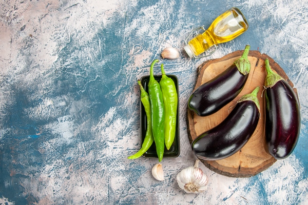 top view eggplants on tree wood board hot peppers on black plate garlic oil on blue white background - Как лучше сохранить продукты?