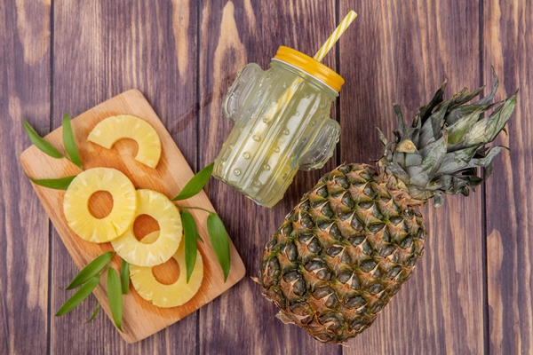 top view of pineapple slices on cutting board with pineapple juice and pineapple on wooden surface - Салат слоёный с ананасом