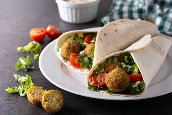 tortilla wrap with falafel and vegetables on black stone background - Фалафель