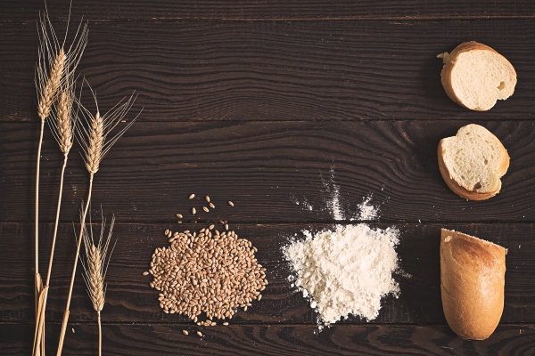 wheat ears grains flour and sliced bread on a dark wooden table top view - О полезном домашнем хлебе