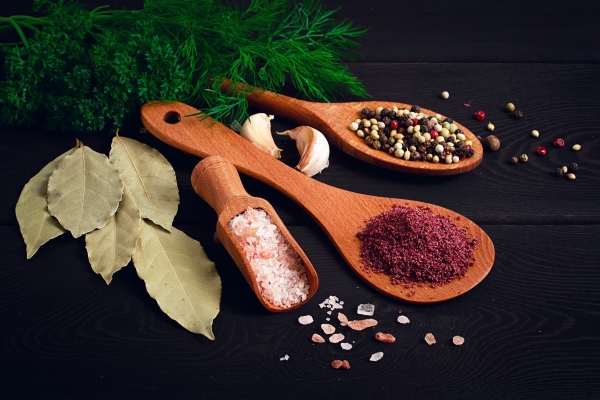 wooden spoons with spices sumac peppercorns pink salt bay leaf fresh herbs on a black wooden table closeup horizontal no people - Консервированный топинамбур