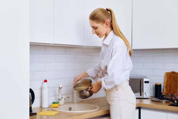 young woman draining cooked spaghetti from water with stainless colander - Крупяные и макаронные изделия: полезные советы