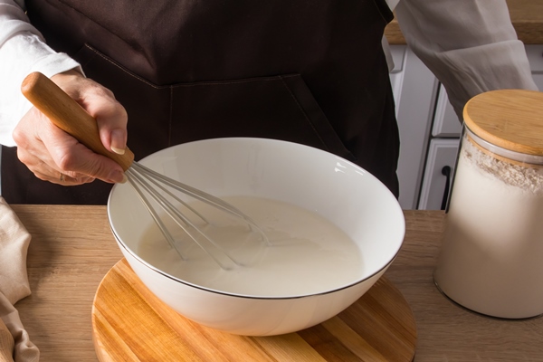 a faceless woman in an apron whisks ingredients in a bowl to make homemade dough wooden table - Постные дрожжевые блины с картофелем