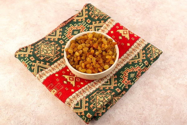a top view orange dried raisins inside round plate on colorful designed carpet on pink - Кулич шафранный