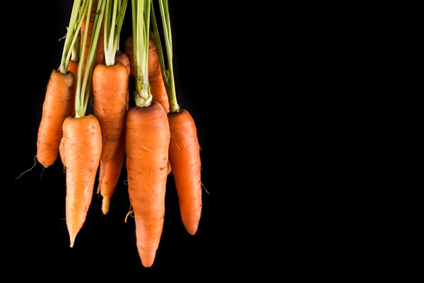 carrots on black background with copy space - Постные блины со сладкой морковью и изюмом