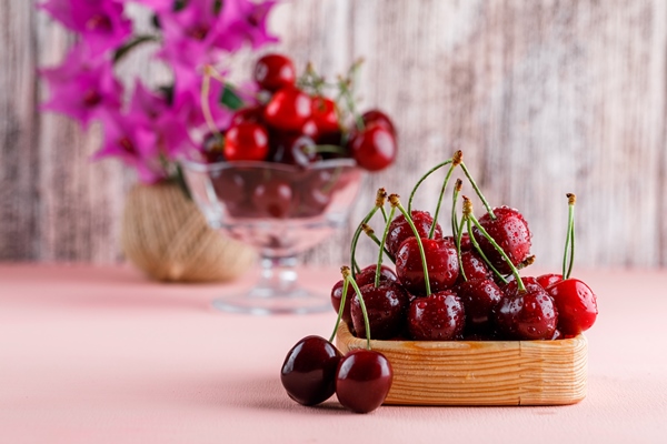 cherries with flower pot in wooden plate and vase on pink and grunge surface side view - Компот из черешни