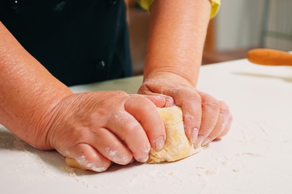 close up of grandmother hands kneading on table in home kitchen retired elderly baker with bonete mixing ingredients with sifted wheat flour kneading for baking traditional cake and bread - Песочный пирог без яиц
