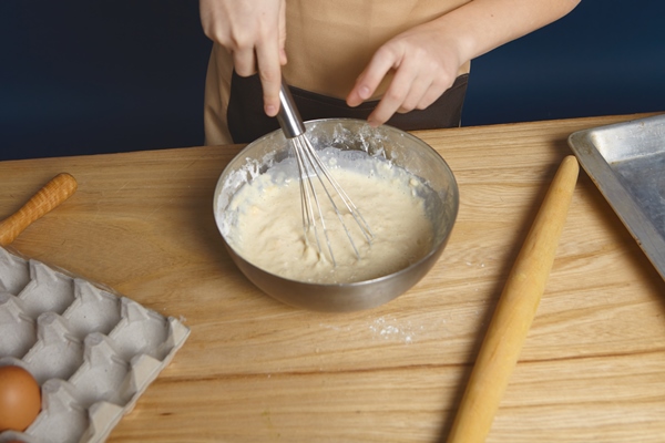 cropped shot of hands holding beater while beating eggs with flour for pine cakes in metal bowl - Кулич пасхальный с изюмом