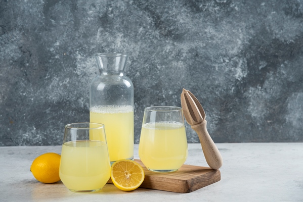 cups full of lemonade with slice of lemon and wooden reamer - Имбирный лимонад