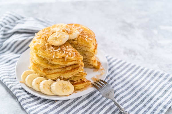 eating freshly baked coconut banana pancakes garnished with sliced bananas and toasted coconut - Постные банановые блинцы на минеральной воде