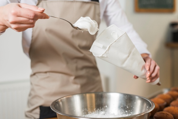 female baker filling whipped cream in the white icing bag - Марципаны на розовой воде