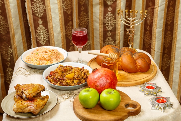 festive table for a meal on rosh hashanah challah honey pomegranate apples wine and traditional chelnt and meat next to the menorah - Библия о пище