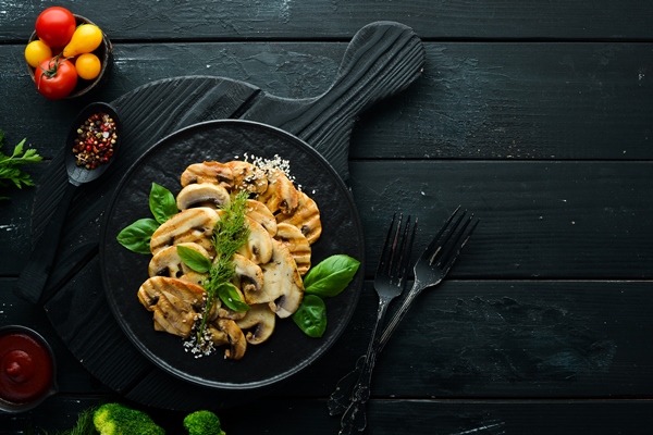 fried mushrooms with sesame and basil in a black plate on a black background top view free space for your - Постные блинчики с гречкой и грибами