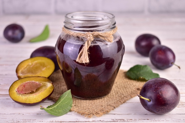 homemade plum jam in a glass jar on a white wooden background - Консервированные сливы с имбирем