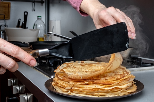 human hands holding a kitchen spatula spread on the dish a freshly baked fragrant pancake from which steam comes home kitchen traditional treat for the holiday of maslenitsa - Постные блины с картофельной начинкой