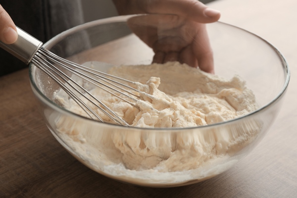 human hands stirring dough with flour in glass bowl on table - Постные блины без масла