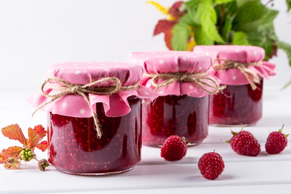 jars with raspberry jam placed in rows and fresh raspberry on white wooden table - Малина в собственном соку