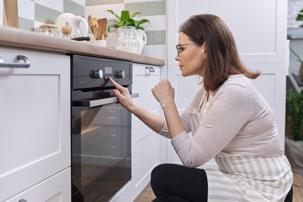 mature woman in apron near the oven in kitchen housewife turning on the settings on stove copy space - Баба нежная