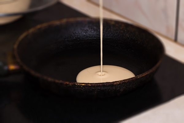 pancake batter baking mix being poured from a bowl onto a hot electric griddle cooking delicious breakfast meal for a family - Постные дрожжевые блины с картофелем