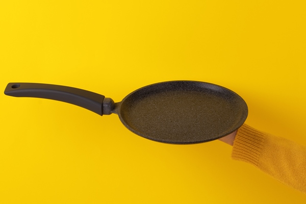 pancake pan utensil on hand over yellow background - Постные банановые блины на минеральной воде