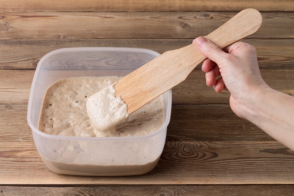 rye sourdough on flour sourdough in a container on a wooden table fermentation the hand holds a wooden spatula the readiness of the sourdough is checked - Кулич с лимонной цедрой