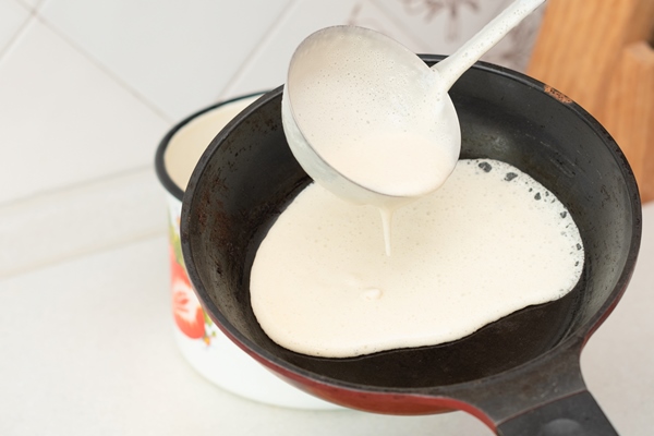 senior woman chef pour portion of liquid dough by hands with ladle on frying pan for baking pancakes 1 - Постные блинчики с гречкой и грибами