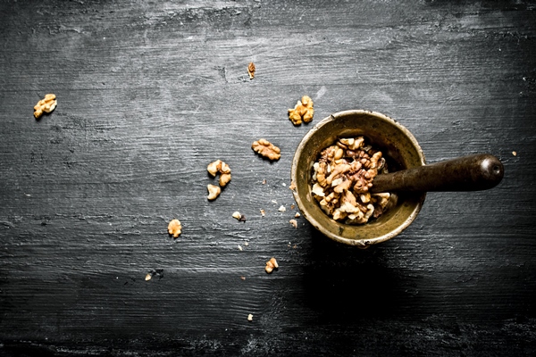 shelled walnuts in a mortar with pestle on black rustic table - Салат из зелени сельдерея с ореховым соусом