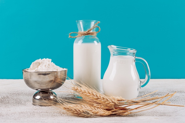 side view bottles of milk with bowl of flour wheat on white wooden and blue cloth background horizontal - Блинцы на кефире с кипятком