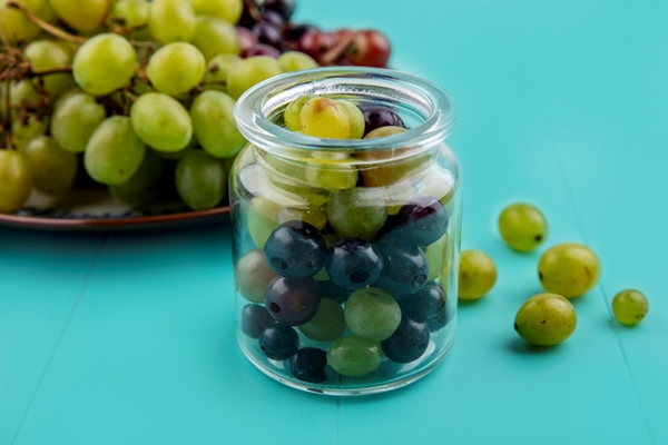 side view of grape berries in jar and grapes in plate on blue background - Маринованный виноград с горчицей