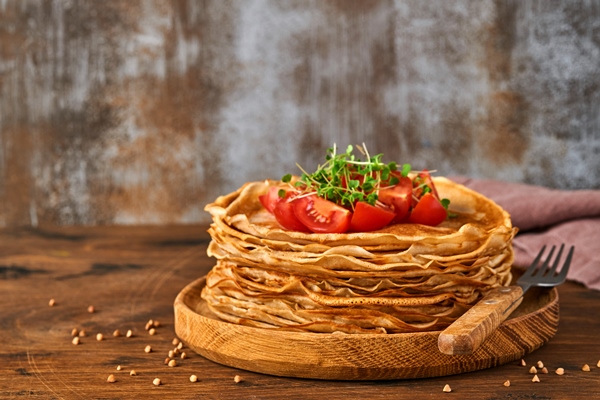 stack of gluten free buckwheat flour crepes pancakes with cherry tomatoes and arugula microgreens on wooden plate homemade healthy baking for breakfast - Блины пшенично-ржаные постные