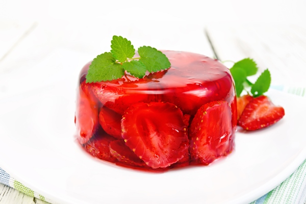 strawberry jelly with mint and berries in a plate on a napkin against the background of wooden boards - Клубничное желе