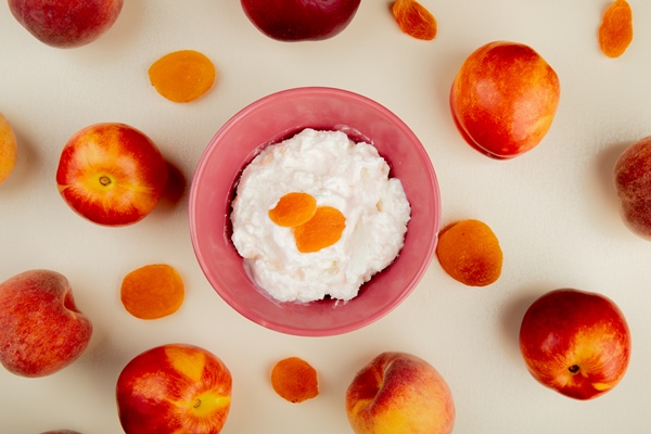 top view of bowl of cottage cheese with raisins and peaches around on white surface - Пасха с курагой 