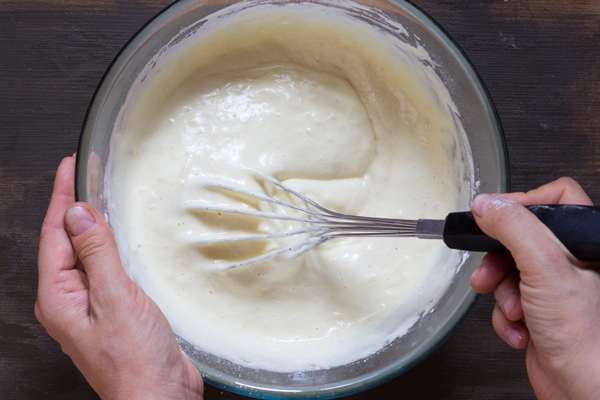 top view of woman hand mixing with whisk dry ingredients and batter on the wooden background - Постные ржаные блины на минеральной воде