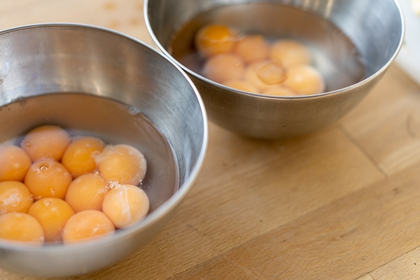 two stainless steel bowls filled with many cracked eggs with whole yolks in the wooden table close up - Пасхальный кулич
